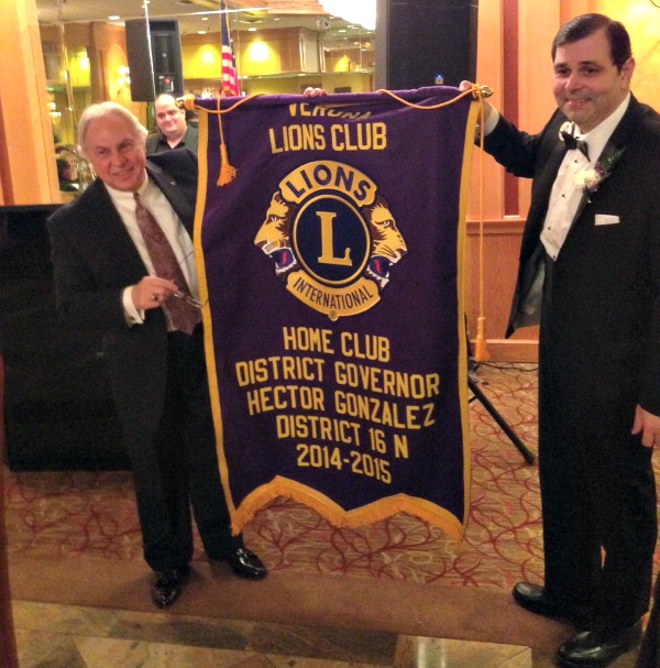 Verona Lions Club President Frank Ricciardi (left) and Lions District 16N Governor Hector Gonzalez (a Verona resident and Verona Lions Club member) proudly display the banner created to commemorate Hector’s extraordinary service to District 16N as its District Governor. 