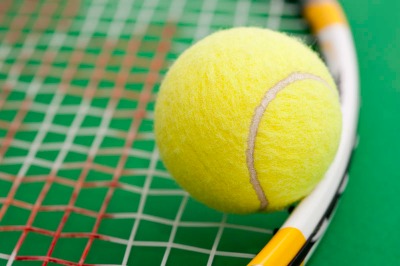 close up on a tennis ball resting on the strings of a tennis racket
